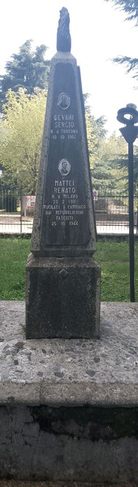 Monumento agli antifascisti, obelisco con dettagli commemorativi e un basamento in pietra, circondato da verde.