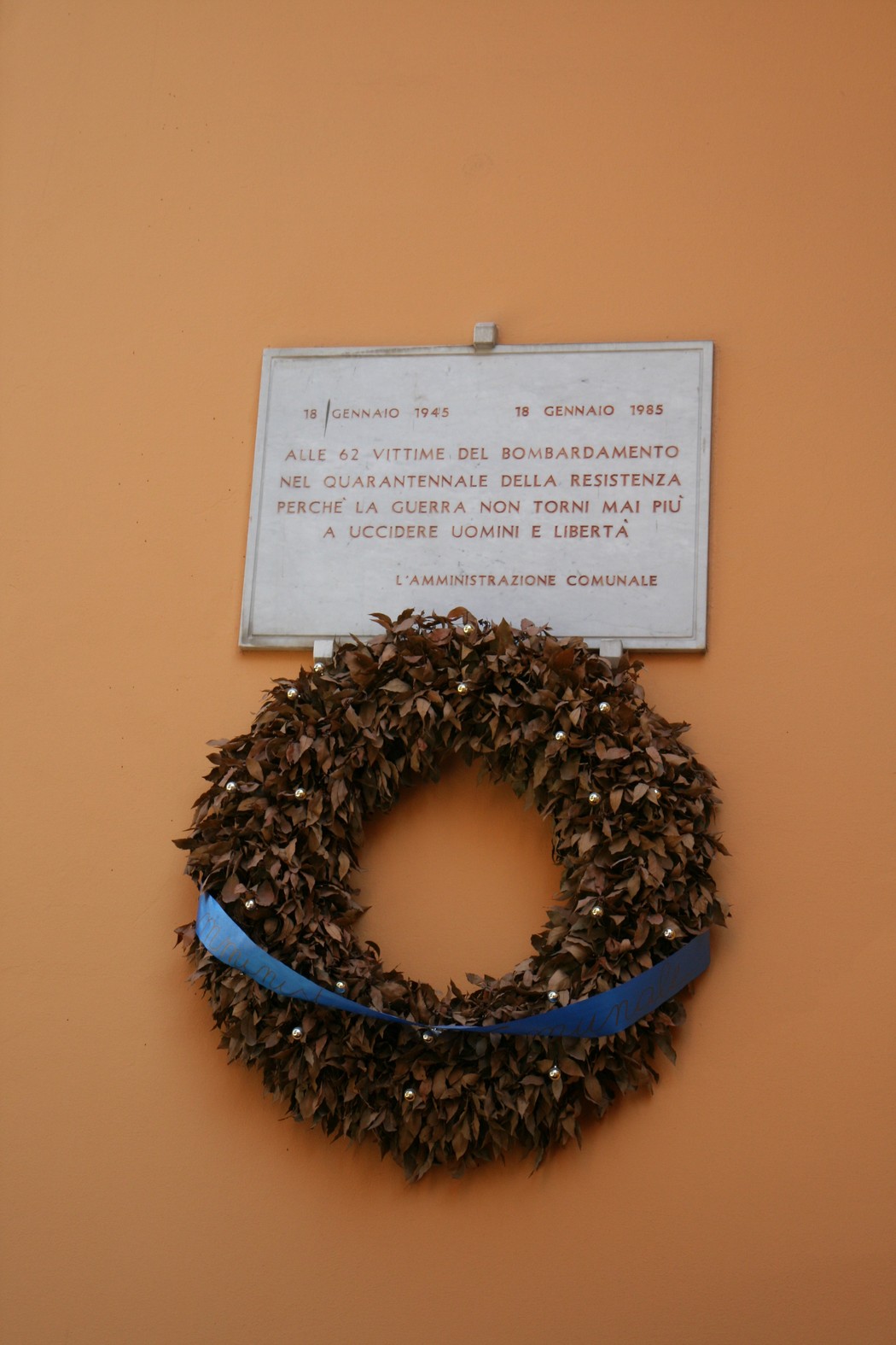 Lapide in memoria delle vittime del bombardamento, con decorazione di alloro e una fascia blu.