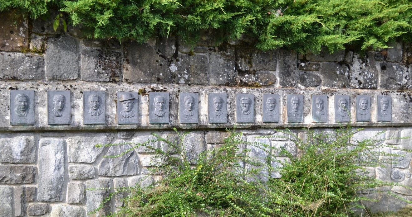 Monumento commemorativo ai partigiani, con medaglioni in rilievo su una parete di pietra.