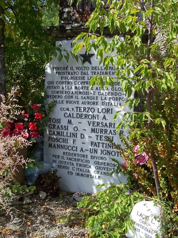Lapide commemorativa che celebra la memoria e il sacrificio, decorata con fiori e simboli di devozione.