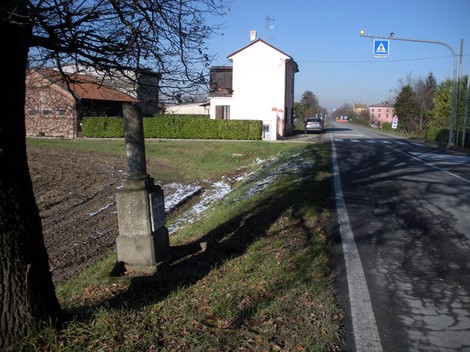 Cippo stradale situato lungo la strada, vicino a edifici residenziali e un campo.
