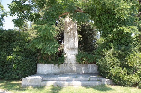Monumento ai militari caduti in prigionia, sormontato da alberi e circondato da siepi verdi.