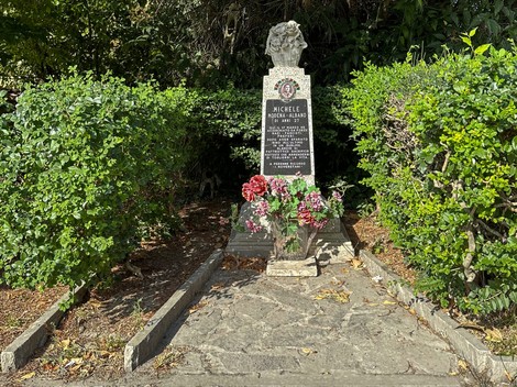 Monumento in memoria di Michele Morrone, circondato da piante e fiori, situato a Modena.