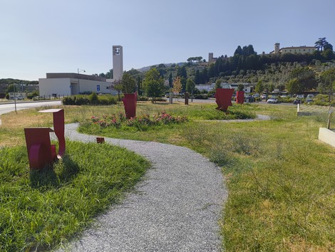 Scorcio di un'opera collettiva che celebra donne resistenti, con sculture rosse in un percorso verde.