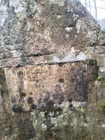 Croce a Paolanti, monumento in pietra con mossi segni del tempo, situato in un contesto naturale.