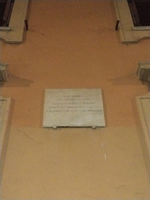 Lapide commemorativa in onore di Simoni, situata su un muro di un edificio storico.