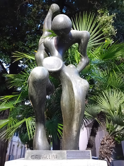 Scultura moderna che rappresenta figure stilizzate, immersa in un contesto di vegetazione lussureggiante.