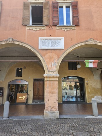 Lapide dedicata ai Partigiani Caduti su una facciata storica con archi e finestre. Bandiera italiana esposta.
