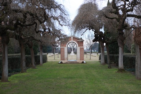 Cimitero di guerra del Commonwealth con alberi e struttura commemorativa in uno spazio verde tranquillo.