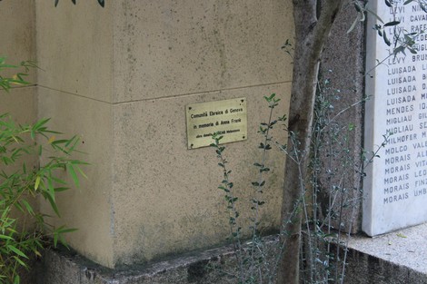 Insegna commemorativa dedicata ad Anna Frank, inserita nel paesaggio di un giardino con vegetazione.