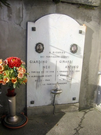 Monumento in memoria dei partigiani caduti, con nomi e date di vita incisi, circondato da fiori.