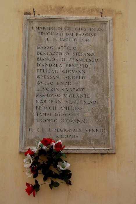 Lapide commemorativa in onore dei martiri di Ca' Giustinian, decorata con fiori, a ricordo delle vittime del fascismo.