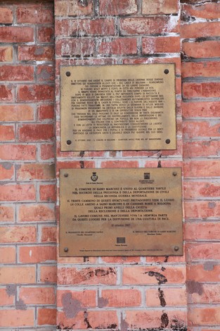 Lapidi commemorative su parete di mattoni, dedicate alla storia delle Caserme Rosse.