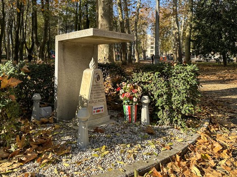 Cippo commemorativo dedicato ai Medici, circondato da piante e fiori, in un parco durante l'autunno.