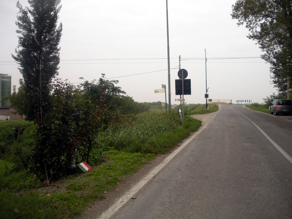 Croce commemorativa ai partigiani di Cascina Bella, situata lungo una strada in un paesaggio rurale.