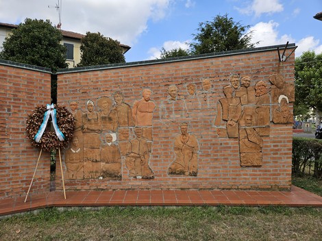 Monumento alla Resistenza con bassorilievi che raffigurano figure storiche e una corona d'alloro accanto.