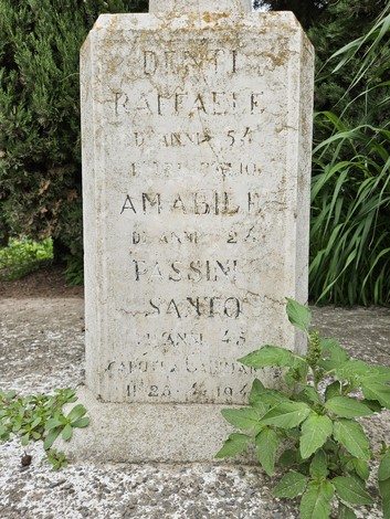Cippo commemorativo con nomi e date di persone scomparse, circondato da vegetazione.