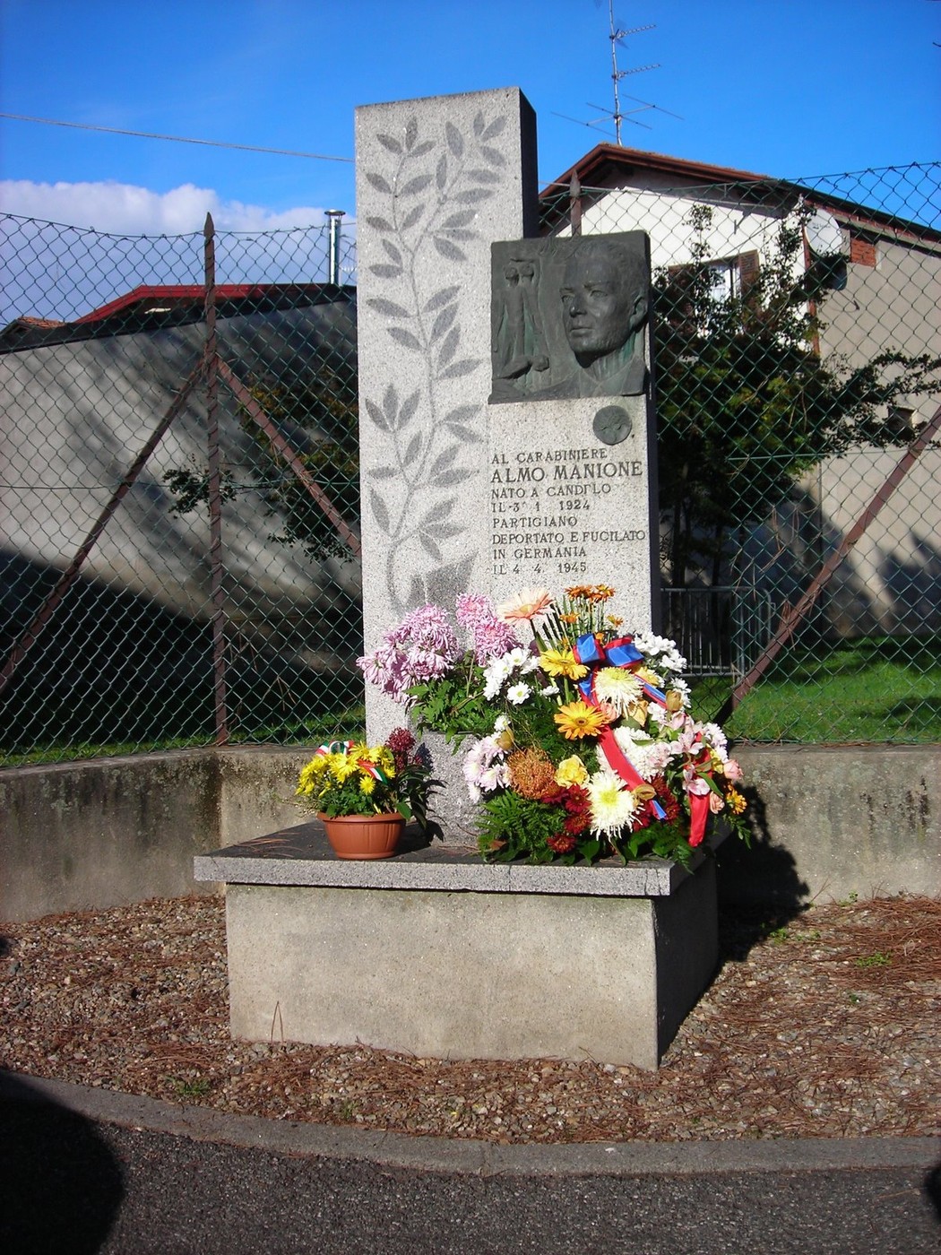Monumento a Manione, dedicato al cap. Almo Martone, adornato con fiori e una scultura commemorativa.