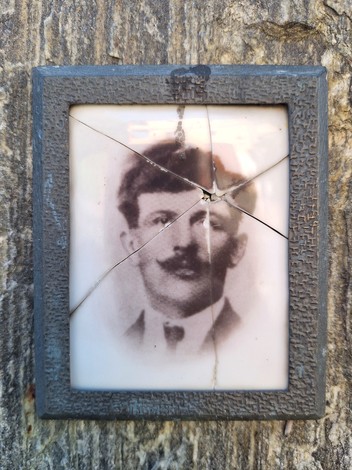 Ritratto di un uomo in una cornice rotta, fissato su un tronco d'albero, che evoca memoria e storia.