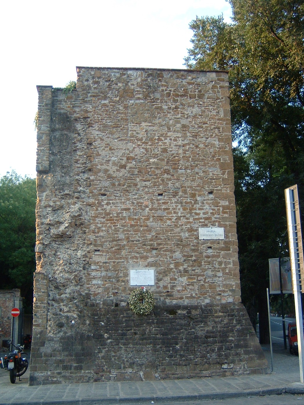 Lapide commemorativa dedicata ai caduti della strage di piazza Tasso, con una cornice di vegetazione.