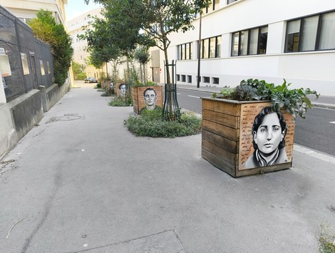 Targhe commemorative del Gruppo Manouchian su fioriere in una strada, con ritratti e messaggi di memoria.