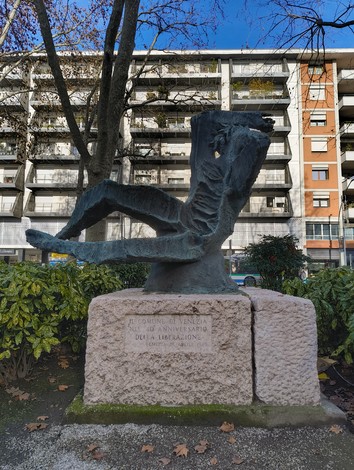 Monumento alla Resistenza, scultura in bronzo con figura stilizzata e base in pietra, immerso nel verde urbano.
