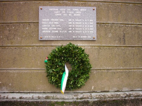 Lapide commemorativa ai fucilati, cimitero di Bellia, con corona d'alloro e tricolore.