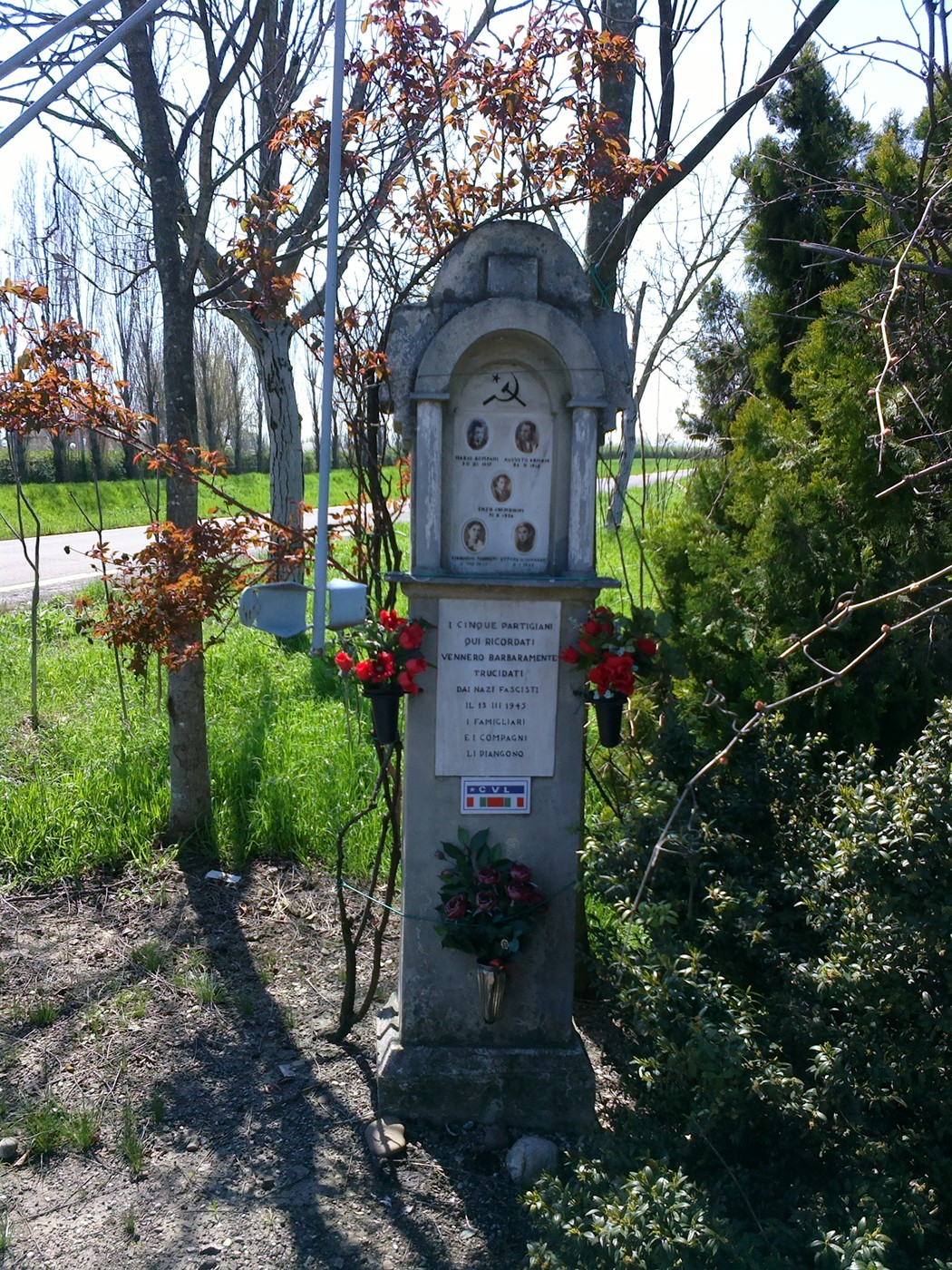 Monumento commemorativo dedicato a Bompani e ad altri, ornato di fiori e situato in un contesto naturale.