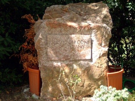 Monumento a Giaconi, un'opera commemorativa in pietra con un design semplice immersa nel verde.
