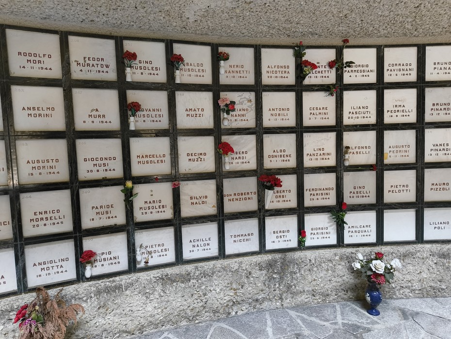 Monumento Ossario dei caduti partigiani, con lapidi in marmo e fiori commemorativi.