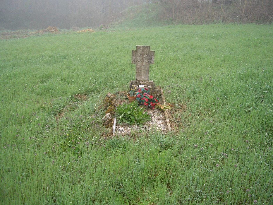 Cippo commemorativo a Laschi, circondato da un prato verde e nebbia, con fiori freschi.