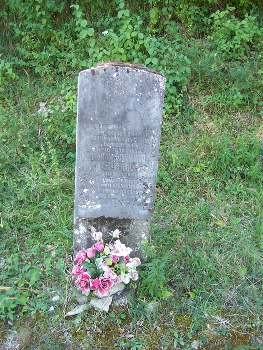 Cippo commemorativo in pietra, adornato con fiori freschi, immerso nel verde naturale circostante.