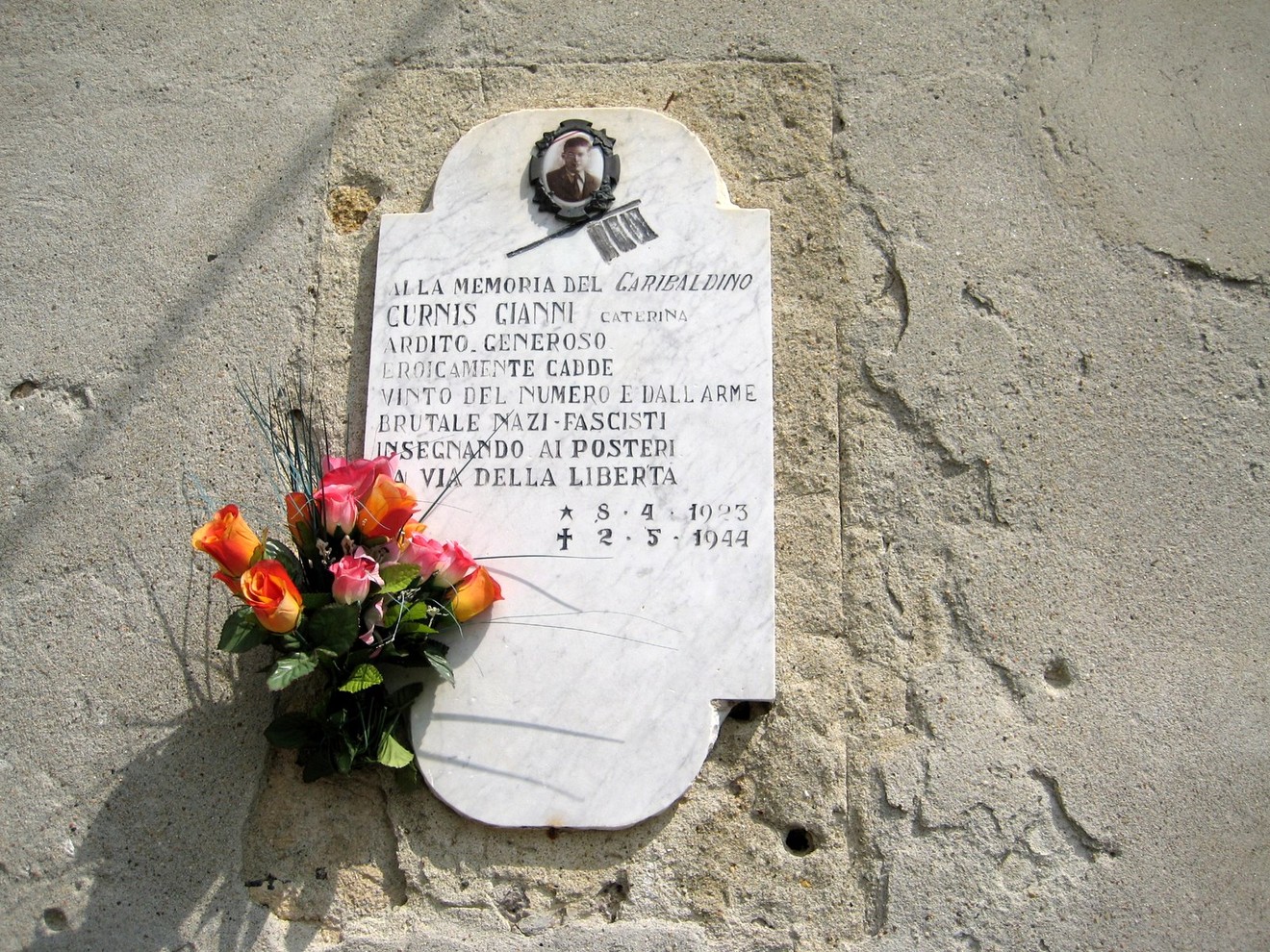 Lapide commemorativa a Curnis in memoria di Gianni Curnis, con fiori e dedica alla libertà.