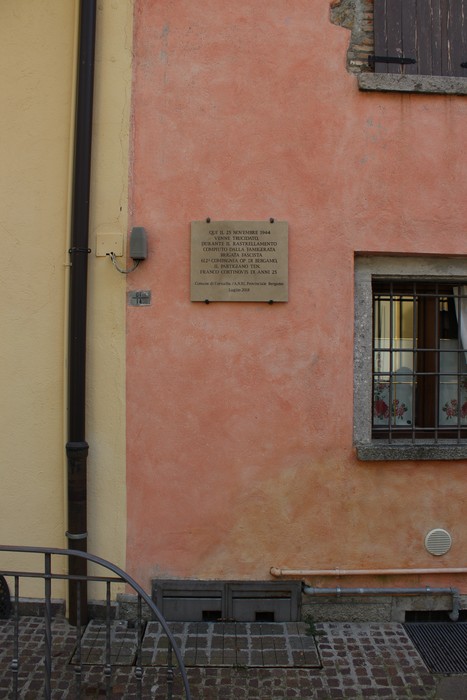 Lapide commemorativa su un muro di colore rosa, con dettagli architettonici in primo piano.