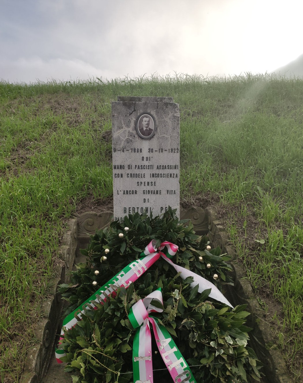 Cippo commemorativo dedicato a Bertoni, con fiori e scritte in ricordo del sacrificio.