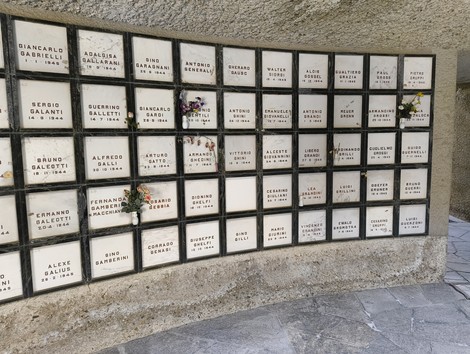 Monumento ossario dedicato ai caduti partigiani, con placche commemorative e fiori.