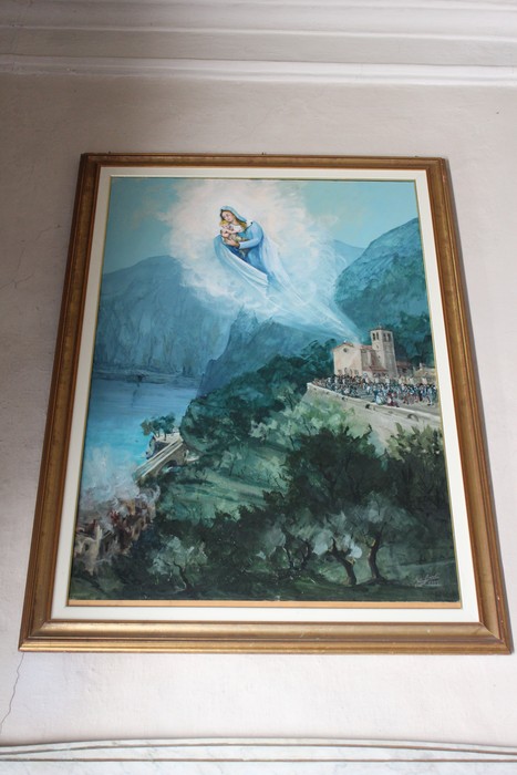 Lapide ex voto che raffigura la Madonna sopra un paesaggio montano e un antico edificio.
