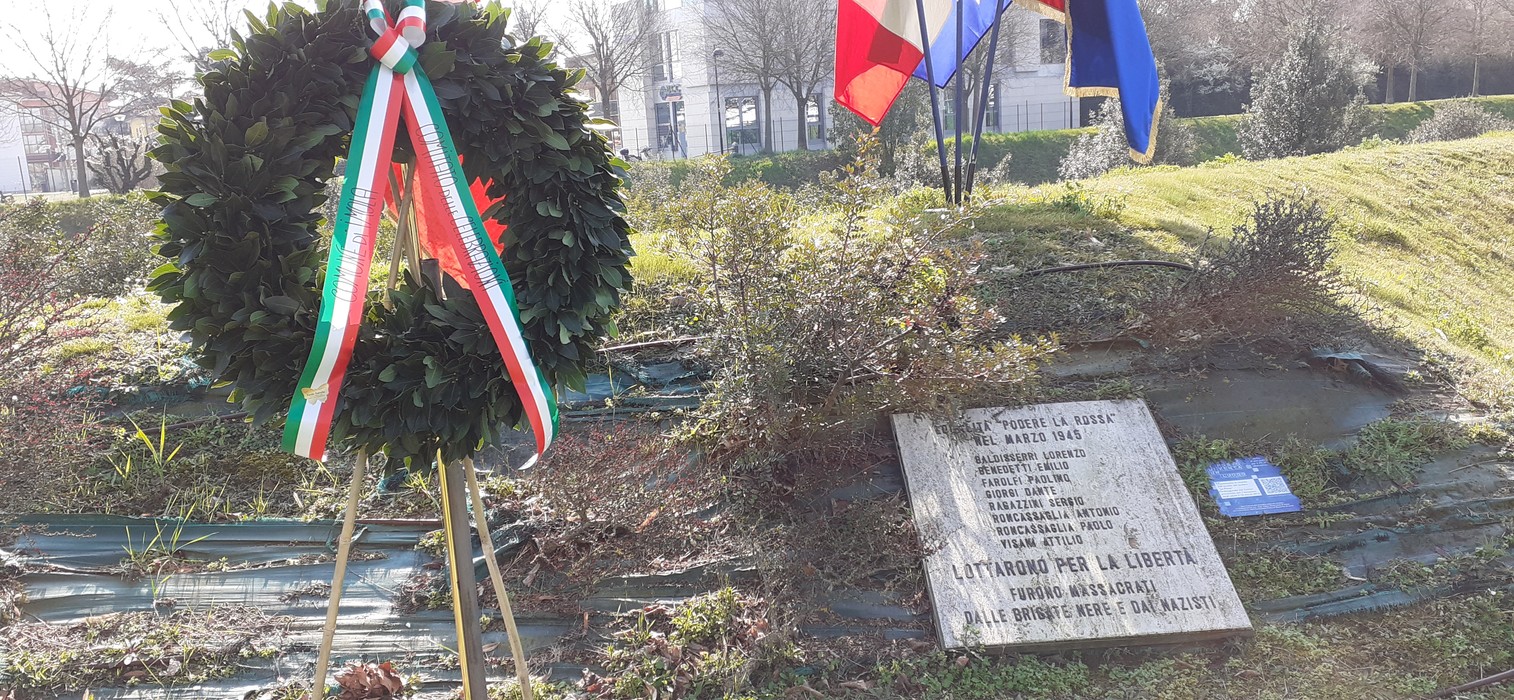 Monumento commemorativo per l'eccidio del podere La Rossa, con corona d'alloro e bandiere.