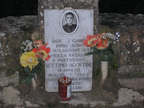 Cippo commemorativo dedicato al partigiano Settimio Agostini, caduto per la patria nel 1944. Fiori e candele adornano il luogo.