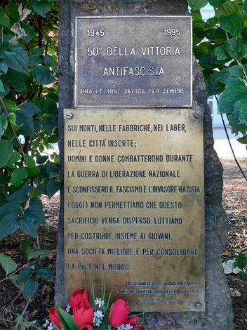 Cippo commemorativo per il 40° e 50° anniversario della Resistenza, con decorazioni floreali e rilievi storici.
