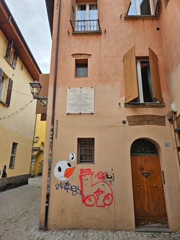 Lapide commemorativa in un vicolo di Bologna, dedicata agli ebrei deportati dal ghetto. Murales colorati sulla facciata.