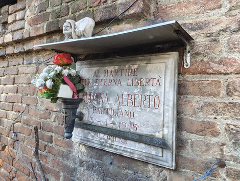 Lapide commemorativa con fiori, dedicata a Alberto Caudana, partigiano, martire per la libertà.