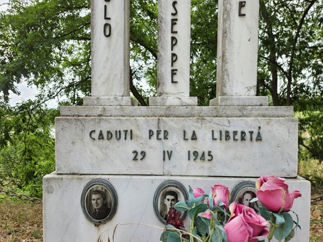 Cippo commemorativo con nomi e fotografie di caduti per la libertà, ornato da fiori in un contesto naturale.