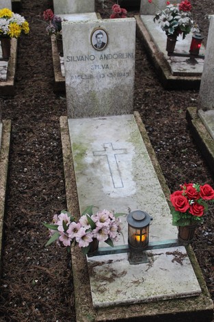 Tombe con fiori e candele dedicate ai caduti per la Libertà, in un cimitero. Atmosfera di rispetto e commemorazione.