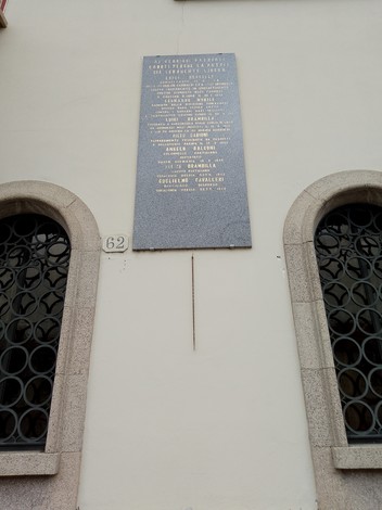 Lapide commemorativa ai partigiani su una parete, con nomi e date in memoria dei caduti.