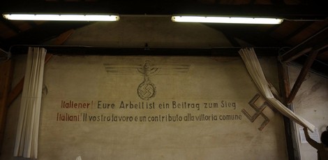 Murale che riinterpreta la propaganda nazifascista, con simboli e testi storici su sfondo grigio.