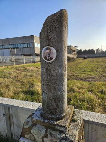 Cippo commemorativo con ritratto, situato in un'area verde accanto a un edificio.
