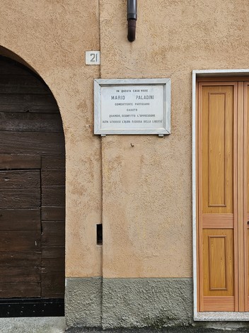 Lapide commemorativa dedicata a Mario Paladini, affissa su una parete in un contesto urbano.