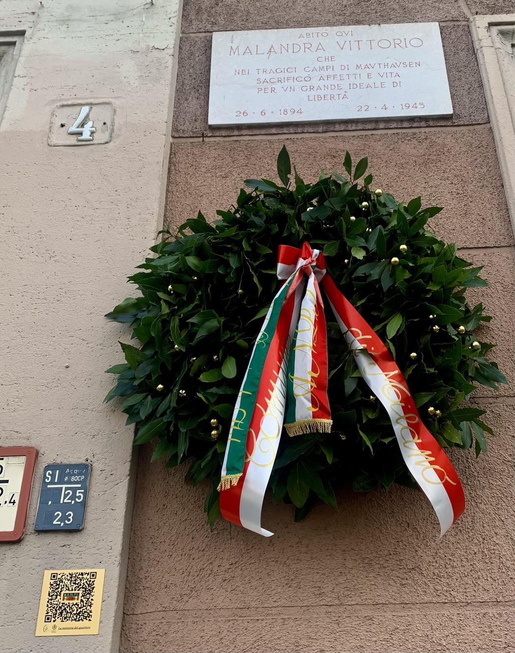 Lapide commemorativa in onore di Malandra, con una corona di alloro e nastri tricolore.