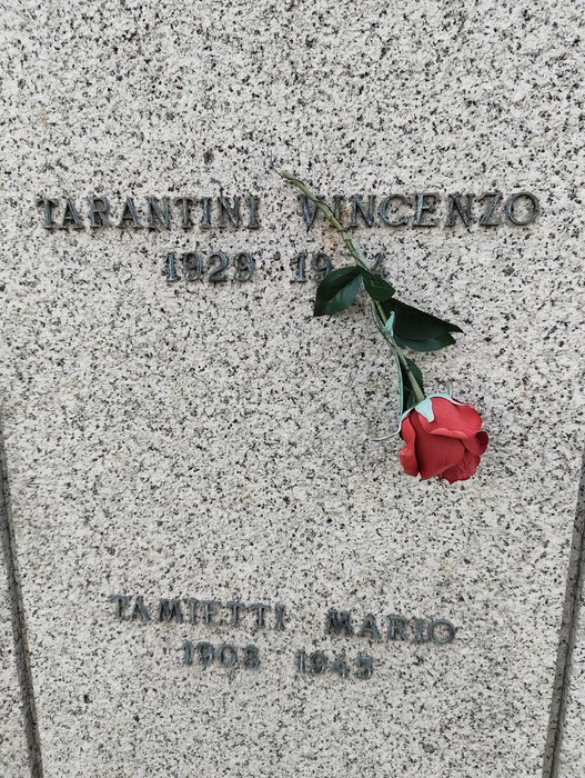 Riproduzione di una targa commemorativa con un mazzo di rose rosse nel Campo della Gloria.